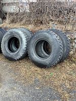 Four tires leaning against a rock wall and brush