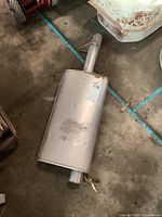 Full view of the rectangular metal muffler with attached pipes, showing minor surface use marks.