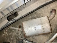 Top view of used automotive muffler lying on concrete floor, showing cylindrical body and integral pipes.