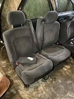 Front view of both driver and passenger side front bucket seats in gray fabric, showing seating surfaces, headrests, and seatbelt attachment points.