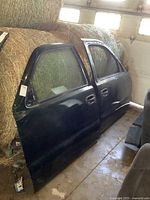Pair of green Chevy truck front doors leaning against hay bales inside a garage, showing full side profiles.