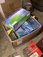 Photo showing unopened boxes of various mixed-brand nitrile gloves stacked in an open case located in a garage or workshop area.