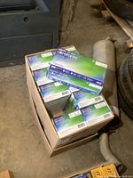 Two cases of unopened boxes of Micro-Flex Ultraform nitrile gloves on a concrete floor with pipes and tires nearby.