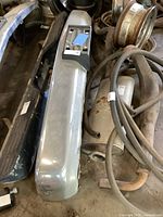 Side view of silver Chevrolet front bumper with minor wear and surrounding automotive parts.