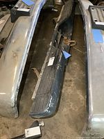 Overall view of used OBS Chevy rear step bumper lying on the floor, showing rubber step pad and metal parts with wear.