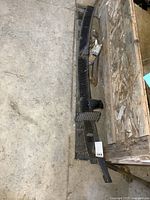 Photo showing long black plastic cowl vent grille piece alongside smaller vent grille pieces and metal wiper motor parts spread on concrete floor near wooden crate.