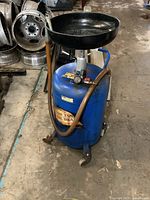 Front angle of blue oil drain tank showing funnel, hose, valve, and wheels.