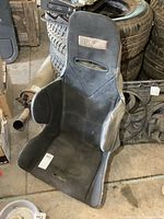 Kirkey racing seat front view showing fabric upholstery, harness slots, and wear.