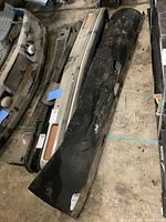 Photo of full width rear mud flap alongside other truck parts on concrete floor, shows surface wear and steel bracket attachment.