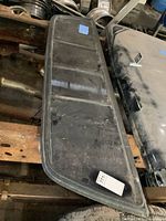 Tinted glass rear sliding window lying flat on a rusty pickup frame.