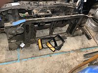 Front view of metal radiator support panel with headlight housings and amber side marker light lenses placed on floor indoors.