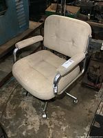 Vintage beige shop chair with chrome armrests and base, showing wear and dirt, positioned on a concrete floor