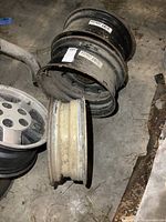 Top view of three steel wheels, two larger 16x6.5 wheels stacked with a smaller 15x5 wheel in front, showing overall used condition with dirt and wear.
