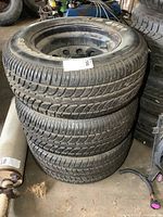 Stack of three 15-inch P245/60R15 tires mounted on black steel wheels with visible tread and dirt.