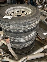 Four stacked white steel wheels with mounted trailer tires in a workshop setting.