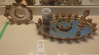 Display of large and small mirrored trays with floral gold borders, tumbler holder, and ornate perfume bottle