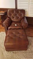 Front view of leather armchair and footstool showing button tufting and nailhead trim