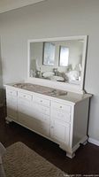 Front view of the white wooden dresser with attached mirror in a bedroom setting, showing drawers and detailed design.
