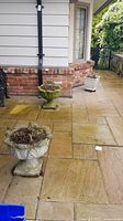 Photo shows three flower pots positioned on outdoor patio against house brick wall, square white pot in background, two large ornamental pots in foreground