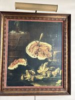 Framed still life painting featuring bread, mushrooms, barrel, and glassware with light fixture mounted on top.