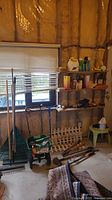 Wide shot of gardening tools stored in a garage workshop with rakes, seed spreader, wooden shelves storing gardening supplies, and various tools visible