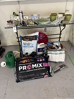 Overview photo shows multiple gardening tools, pots, soil bags, gloves, and watering can on and under glass table