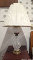 Full view of one glass table lamp with pleated white fabric shade on a wooden surface, showing overall lamp shape and pattern.