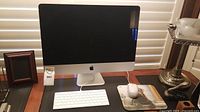 Front view of silver aluminum iMac on desk with display off, Apple logo visible, paired with white wired keyboard and mouse on mousepad
