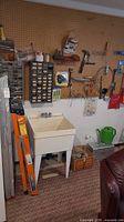 Front view showing orange fiberglass ladder, utility sink and pegboard with various tools and hardware items
