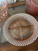 Close-up of a round pink glass dish with four compartments on a textured plate underneath.