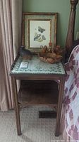 Side view of wooden side table showing decorative cloth on glass top and items placed on it, framed butterfly art in background