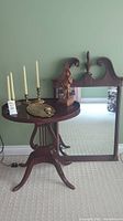 Full view of side table with wooden sculpture and four brass candleholders, wood tray, and tall mirror framed in wood behind