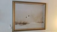 Front view of framed painting showing ducks flying over marsh landscape in soft neutral tones.