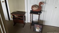 Two wooden tables, one a magazine rack style, the other a taller side table with carved wooden duck on top and framed 'coffee' sign leaning against it.