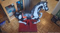 Full side view of the rocking horse on a red wooden base showing black and white paint and tack details.