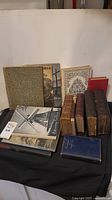 Photo showing the full set of 11 antique books laid out on a black cloth background, displaying various sizes and condition.
