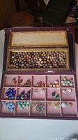 Open box showing top compartment with clay marbles and bottom pink felt tray with glass marbles.