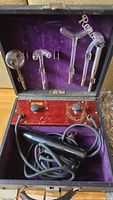 Photo of open violet ray machine case showing wooden control panel, knobs, power cord, and multiple glass electrodes secured in lid.