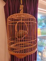 Full view of the antique bamboo bird cage, showing cylindrical shape and dome top with hanging carved wooden bird inside.