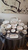 Full set of vintage AK Carlsbad Austria china arranged on a round table showing cups, saucers, plates, serving dishes, and trivets with floral and gold accents.