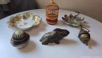Full view of all items including the wooden cage with the Sankyo musical bird, porcelain hare bank, Nippon plates, incense dish and brass bell on table surface.