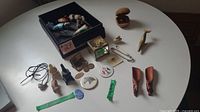 Overview of many netsuke toggles, miniatures, carved ducks, coins, pins, and small collectibles laid out on a white table.