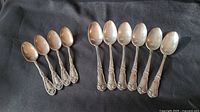 4 Oxford Silver Plate Narcissus teaspoons and 6 Oneida Reliance Plate soup spoons on black fabric background, showing all spoons.