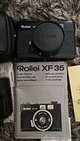 Top view of Rollei XF 35 camera with lens cap and instruction manual underneath