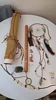 Overview of all items on round white table showing dreamcatcher, flute, soapstone carving, arrowhead, necklaces, and small pipe