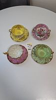 4 Royal Sealy teacups and saucers in yellow, pink, and green colors arranged on white surface.