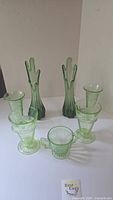Full set of eight green uranium glass items displayed: four footed glasses, two tall vases, sugar bowl, and another glass.