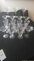 Front view of 18 assorted Morgantown vintage glasses showing footed tumblers and champagne glasses set on a black cloth surface.