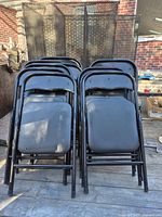 10 black folding chairs stacked in two groups, showing metal frames and cushioned seats.