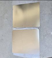 Two flat metallic sheets of sheet metal stacked with reflective silver surface visible on top.